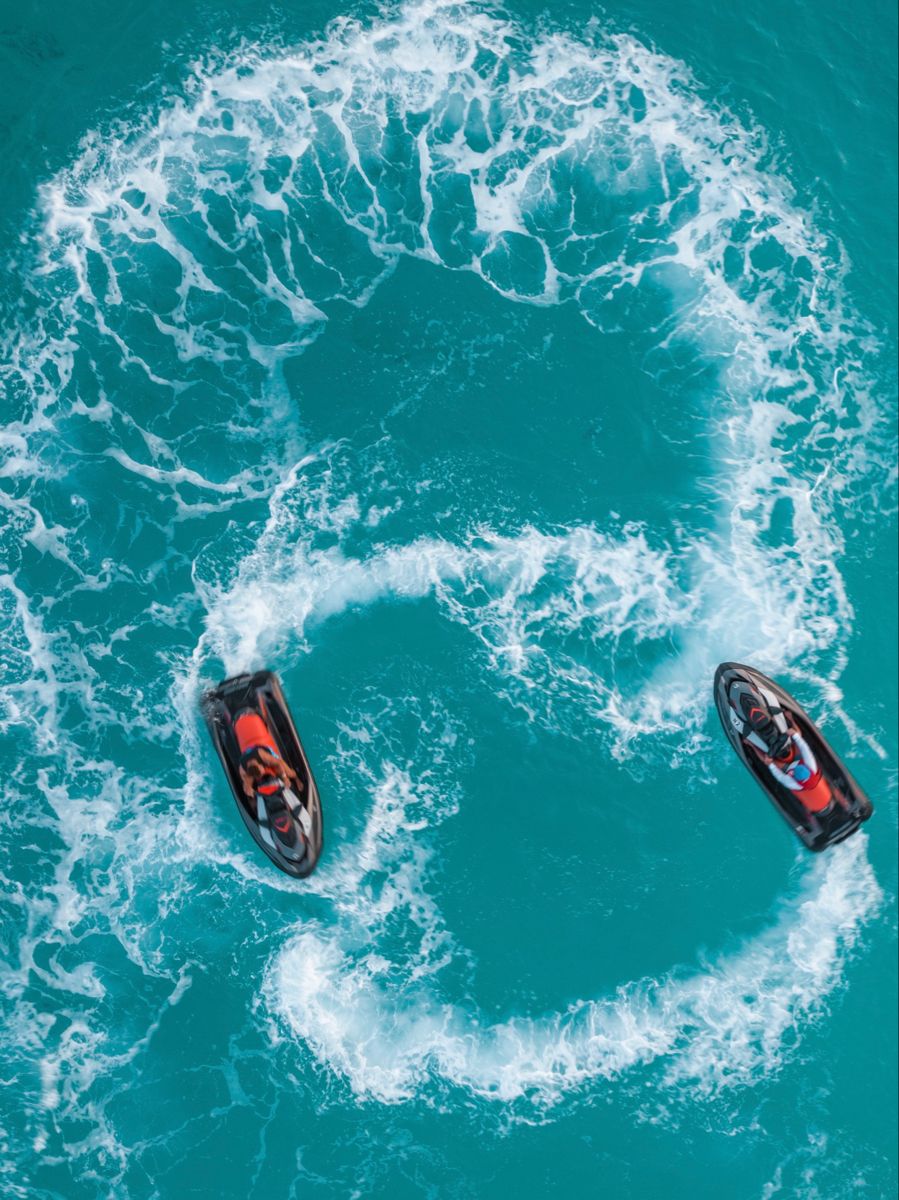 Dois jet skis desenhando círculos em água turquesa, vistos de cima